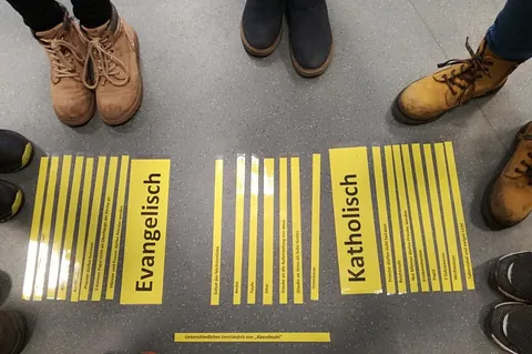 Füße von Menschen um ein Bodenbild zur Ökumene